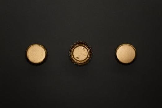 A flat lay showing three gold bottle caps on a black surface, perfect for template and design use.